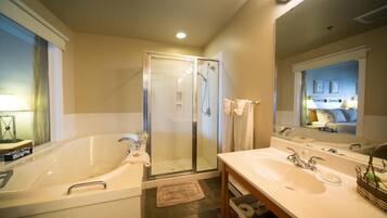 A modern bathroom with a large bathtub, a walk-in shower, and a vanity with two sinks.