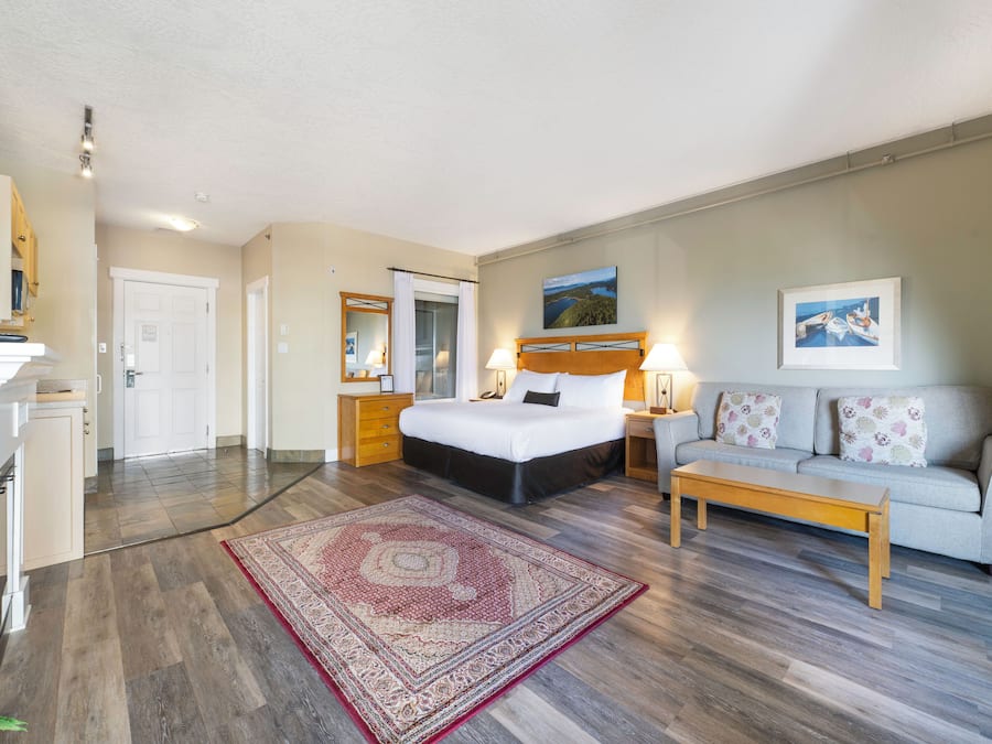 A hotel room with a bed, a sofa, a coffee table, a TV, and a large window.