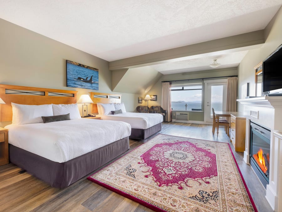 A hotel room with two beds, a fireplace, a television, and a large window with a view.
