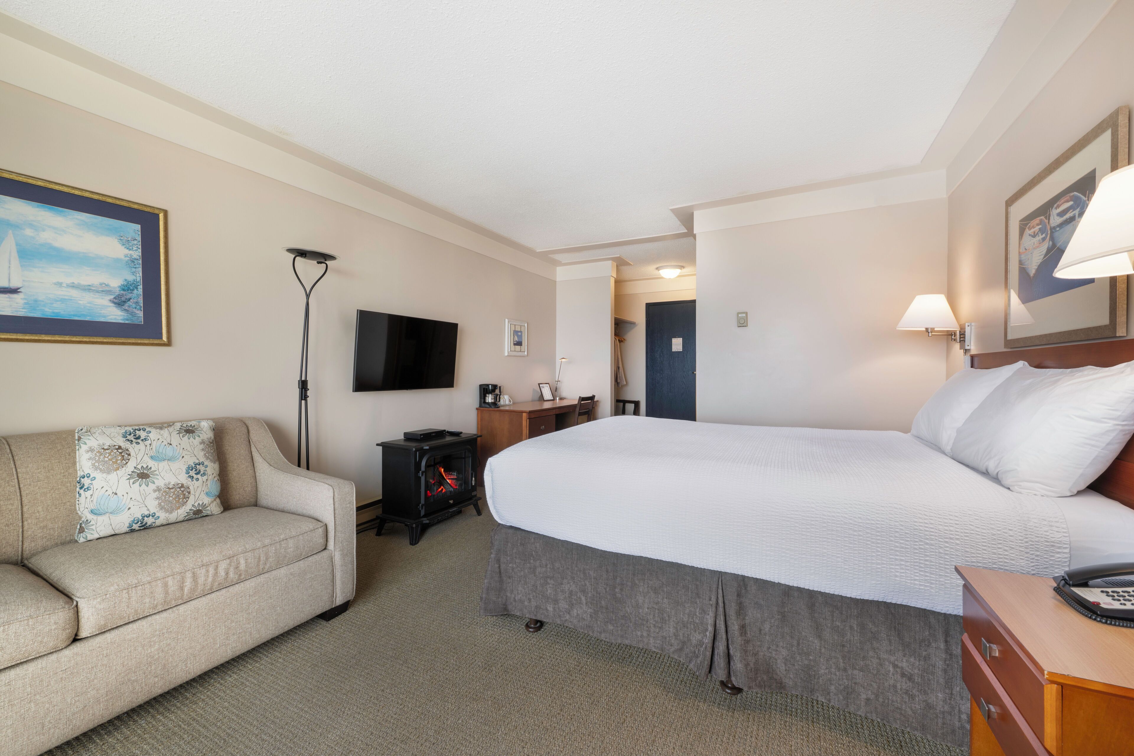 Una habitación de hotel con cama, sofá, televisor, escritorio y chimenea.