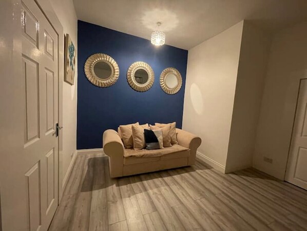 A room with a blue accent wall, a beige sofa, and three decorative mirrors. - COSY HLA HOLYTOWN APARTMENT (Bellshill)