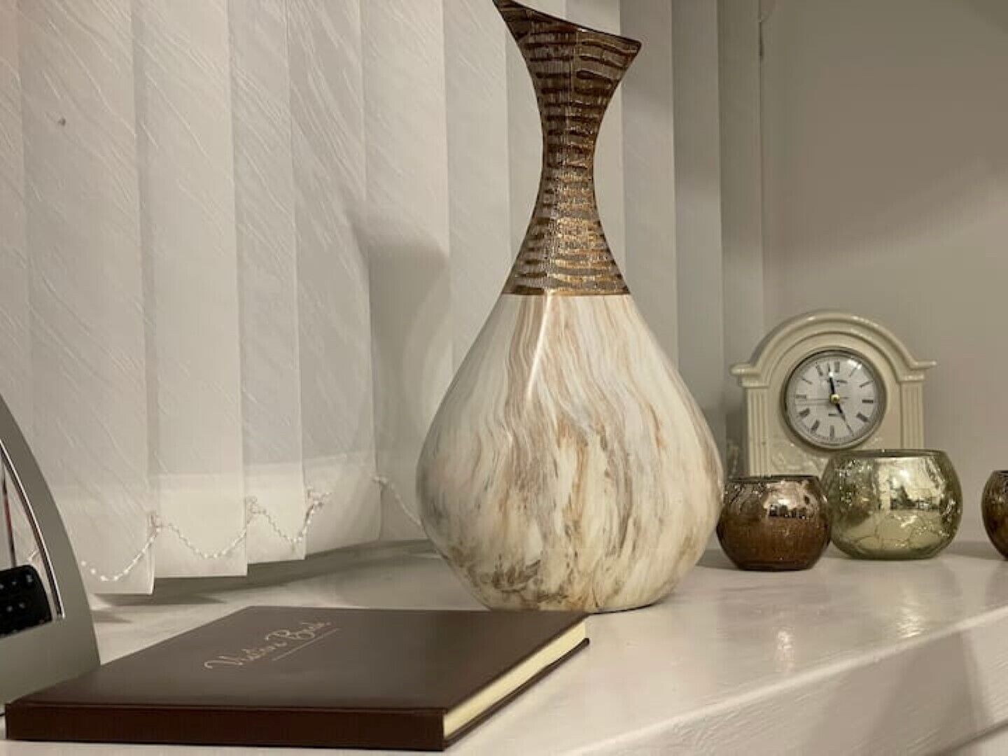 Un vaso in marmo, un orologio e altri vasi decorativi su uno scaffale.