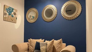 A beige sofa with multiple cushions against a dark blue wall, flanked by three decorative mirrors with a golden frame. - COSY HLA HOLYTOWN APARTMENT (Bellshill)