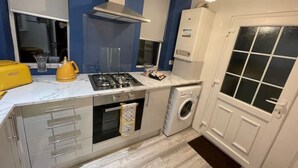 A compact kitchen with a gas stove, oven, microwave, and a built-in washing machine. - COSY HLA HOLYTOWN APARTMENT (Bellshill)