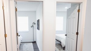 Un pasillo que conduce a un dormitorio con una cama, una lámpara de pie y una alfombra.