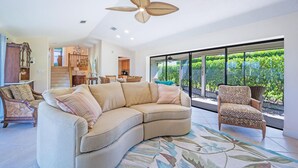 Un salón espacioso con un sofá seccional curvo, un sillón estampado y un ventilador de techo.