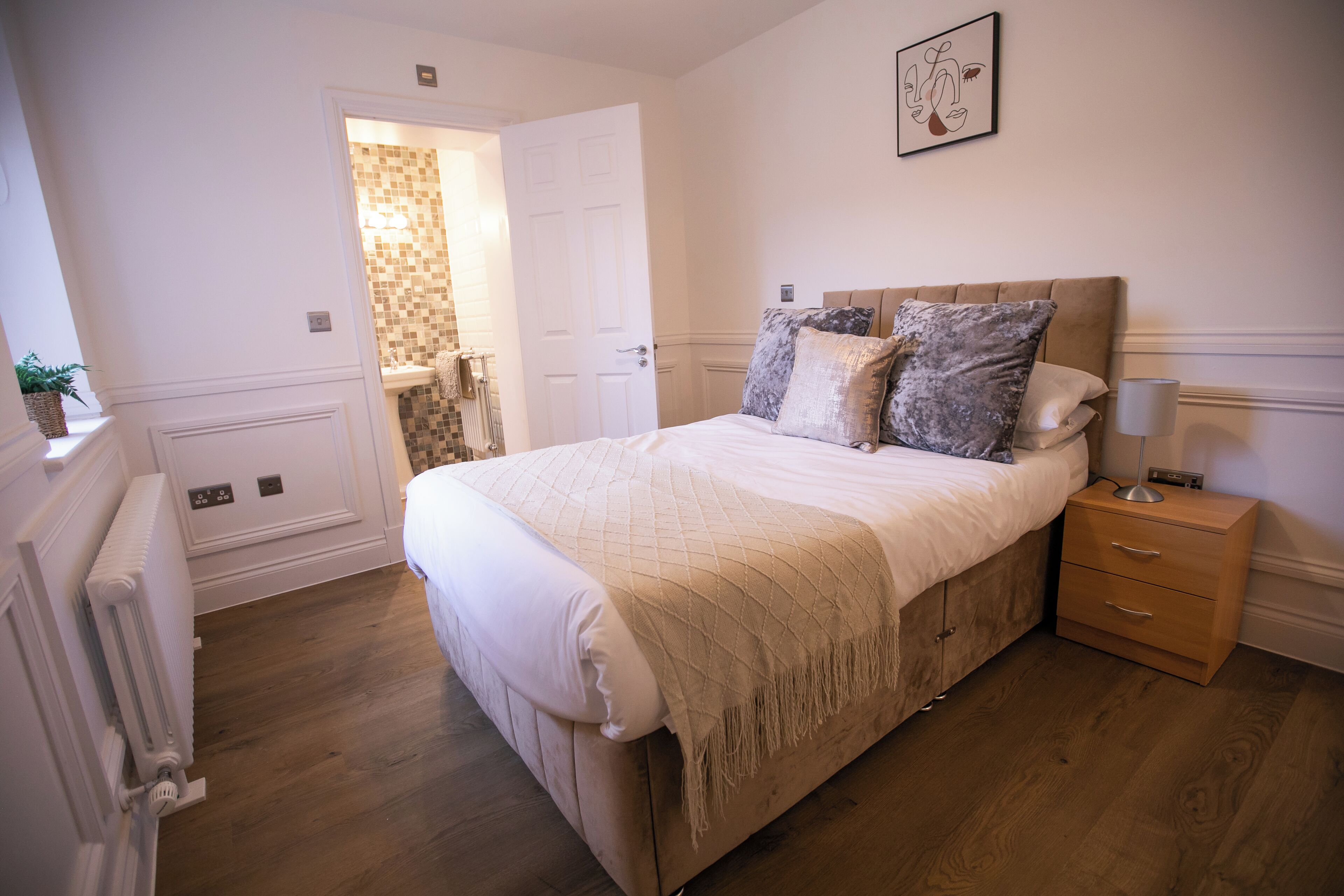 A bedroom with a large bed, a bedside table, a radiator, and a door leading to a bathroom.