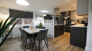 A modern kitchen with a central island, dark cabinetry, and a dining area with a table and chairs. - The Burlington Collection (Sheringham)
