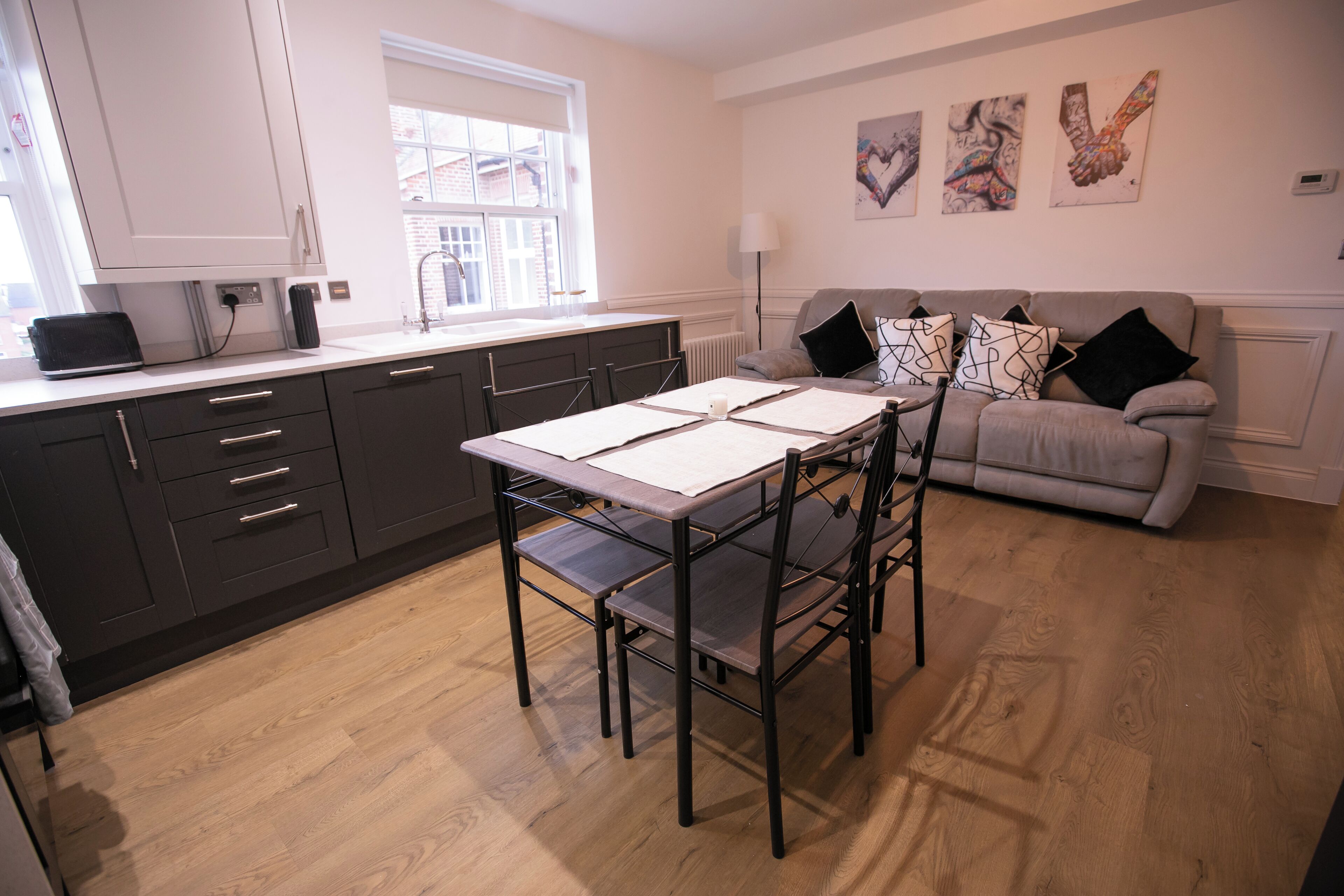 A modern kitchen with a dining table and chairs, a grey sofa, and artwork on the wall.