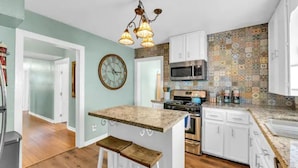 A kitchen with a central island, white cabinets, a microwave, stove, and a clock on the wall.