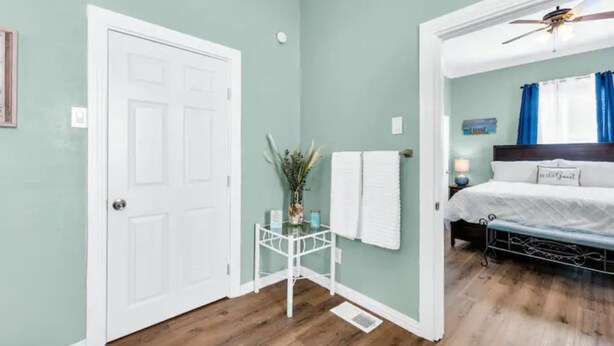 A bedroom with a bed, a nightstand, a ceiling fan, and a door.