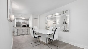 Una cocina moderna con armarios blancos, un refrigerador de acero inoxidable y una barra con taburetes.