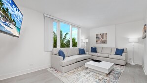 Una sala de estar moderna con un sofá color beige, una mesa de centro y una pantalla grande mostrando una escena de playa.