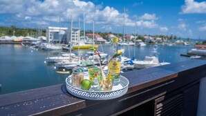 Ein Tablett mit Rum, einer Limette und einem Gewürzglas auf einem Balkon mit Blick auf einen Yachthafen, der Boote und Gebäude zeigt.
