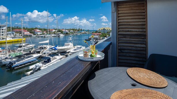 Ein Balkon mit Blick auf eine Marina, ein Tisch mit geflochtener Unterlage und eine Wasserflasche.