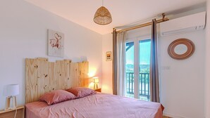 A bedroom with a wooden headboard, a bed with pink bedding, a bedside lamp, and a view of a balcony. - La Terrasse - Three Bedroom House, Sleeps 6 (La Teste-de-Buch)