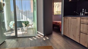 A modern kitchen with wooden cabinets, a dining area with a table and chairs, and a sliding glass door leading to a balcony.