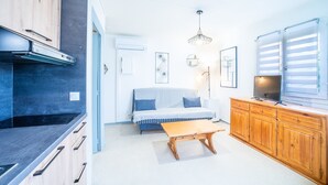 A compact living space with a kitchenette, a sofa, a wooden table, and a TV.