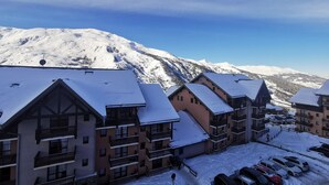 A snow-covered mountain with a clear sky. There are buildings with balconies and a parking area with cars.