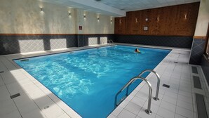 An indoor swimming pool with clear blue water, tiled floor, and wooden panel walls.