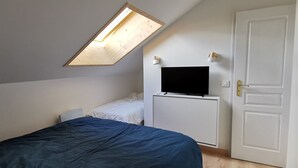 A bedroom with a sloped ceiling, a skylight, a bed, a white wardrobe, a television, and a door.