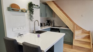 A modern kitchen with a white countertop, grey cabinets, and a wooden staircase.