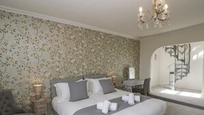 A bedroom with a large bed, a desk, a chair, a chandelier, and a staircase. - Holmere Bank (Carnforth)