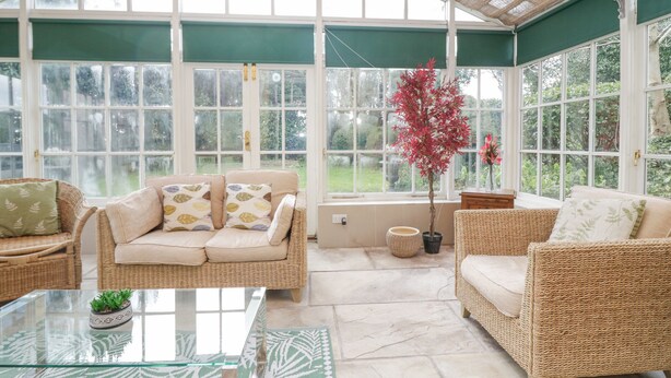 A conservatory with wicker furniture, large windows, and a potted plant. - Holmere Bank (Carnforth)