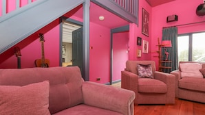 A pink-themed living room with a staircase, a guitar, and a lamp. - Holmere Bank (Carnforth)