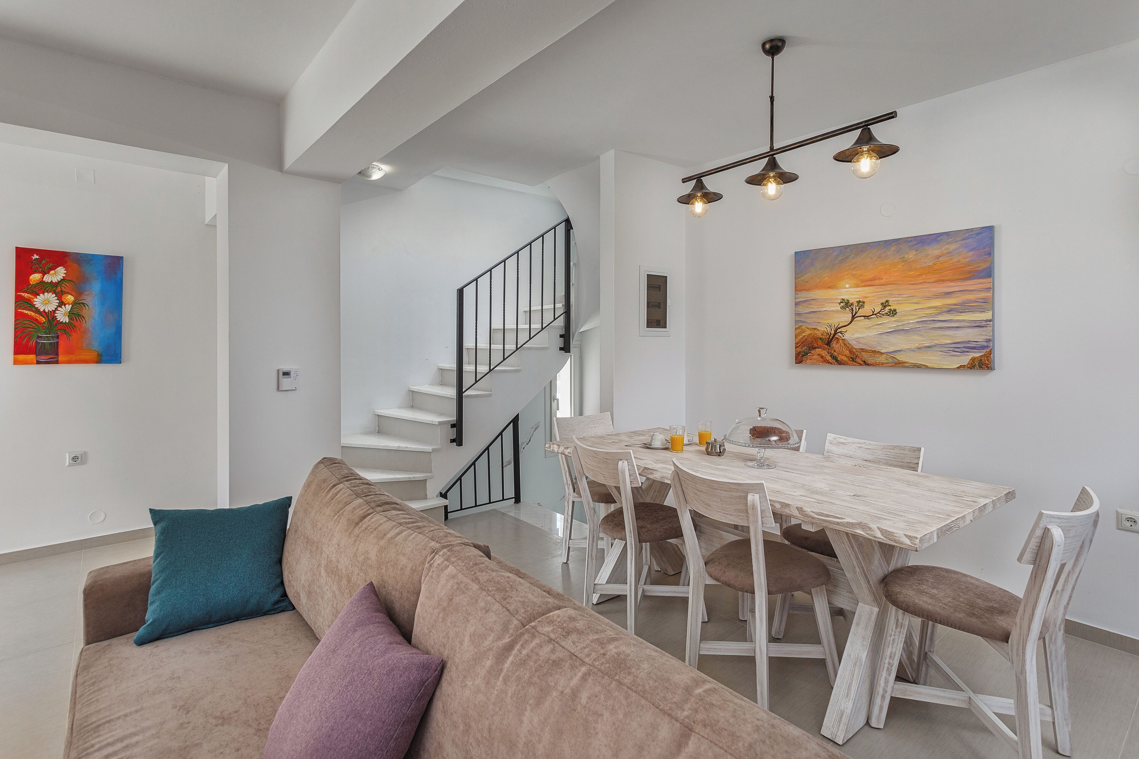 A modern living room with a sofa, a dining table, and chairs. There is a staircase leading to another level.