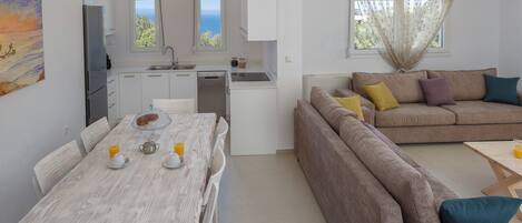 A compact living space with a dining table, kitchen area, and a sofa with cushions.