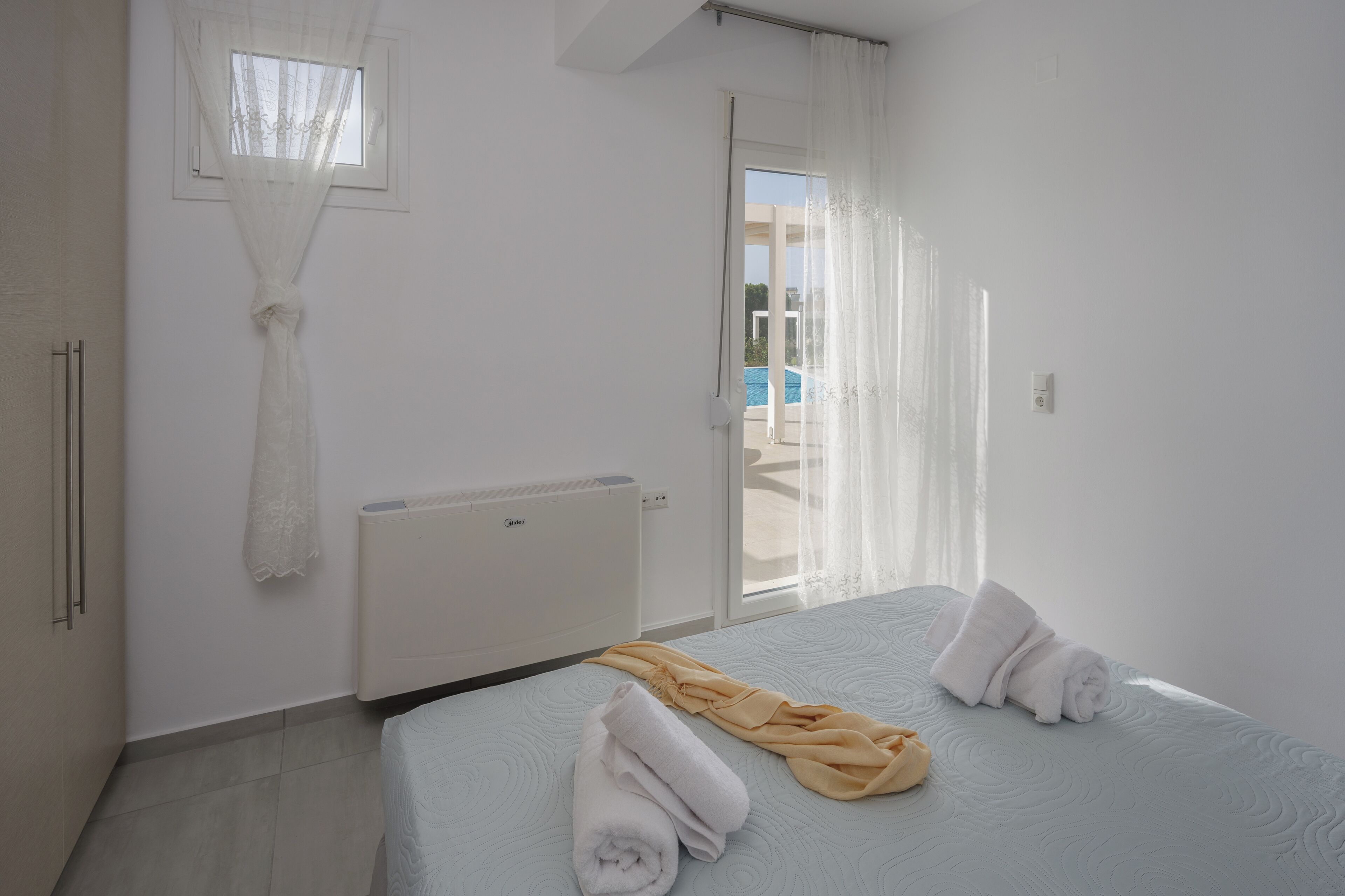 Une chambre à coucher avec un lit, un radiateur, une fenêtre avec des rideaux légers et une vue sur une piscine à l’extérieur.