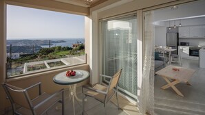 En balkon med et bord og stole, havudsigt og et kig ind til et moderne køkken.