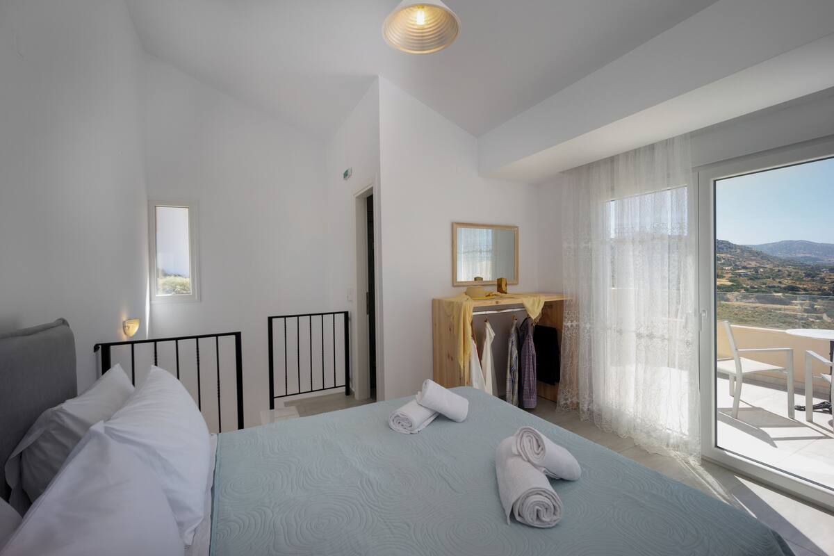 A bedroom with a bed, a bedside table, a mirror, a wardrobe, and a balcony with a view.