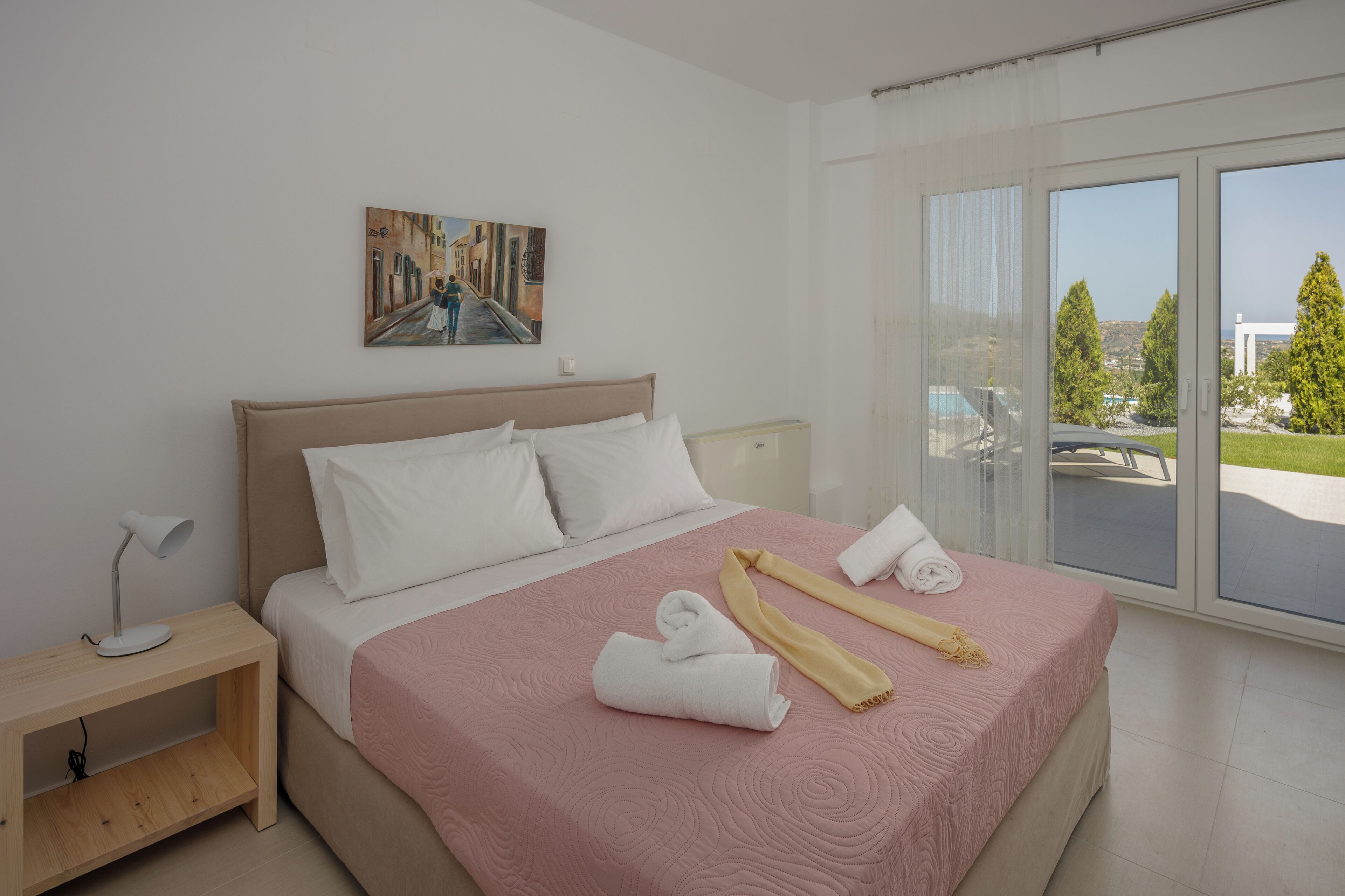 A modern hotel room with a large bed, a painting on the wall, and a view of the outdoors through the sliding glass door.