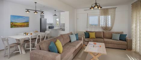 A modern living room with a beige sofa, a wooden coffee table, and a dining area with a white table and chairs.
