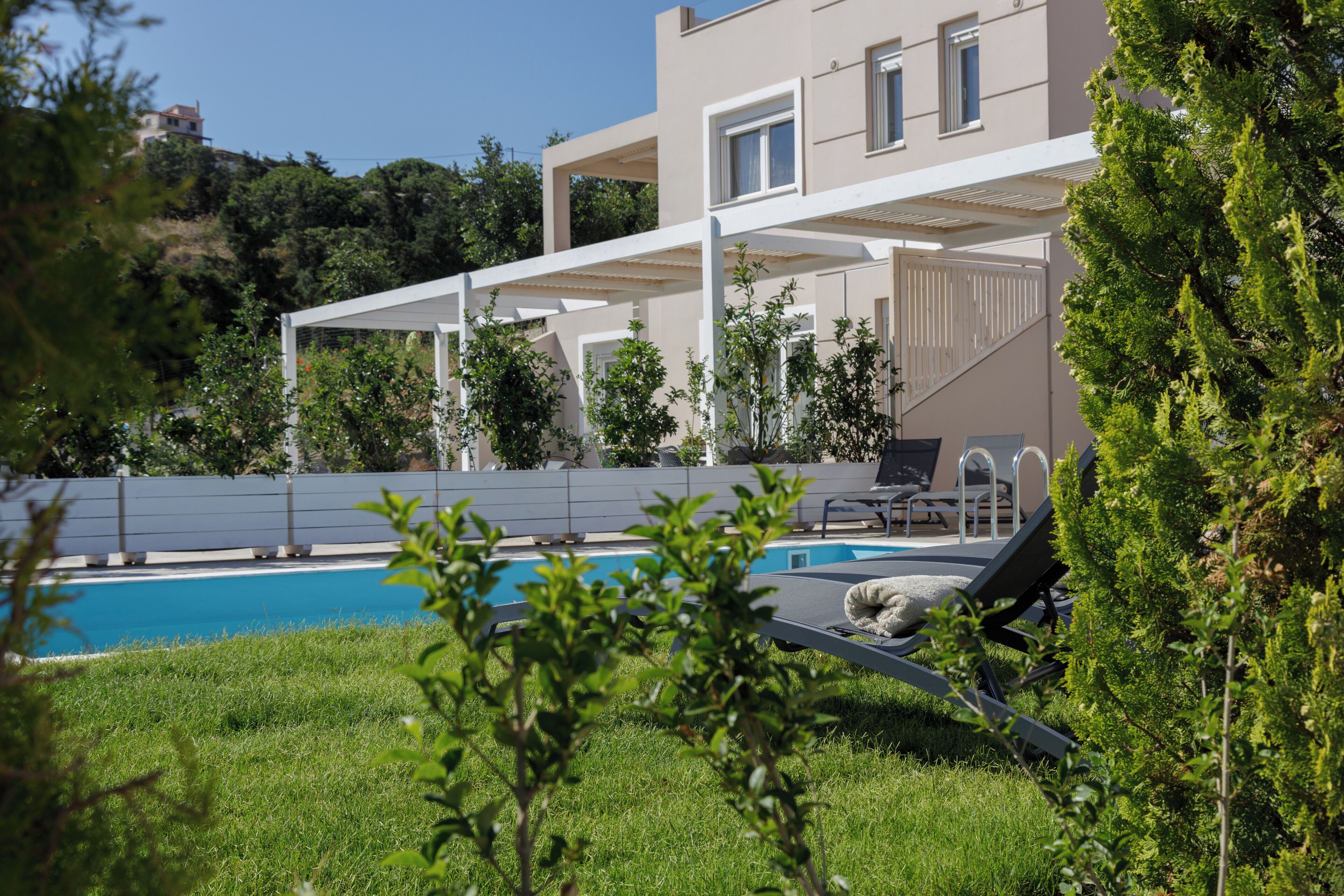 A modern two-story house with a swimming pool, outdoor seating, and a view of a hillside.