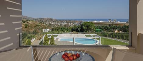 A balcony with a view of a swimming pool, a bowl of fruit, and a distant landscape.