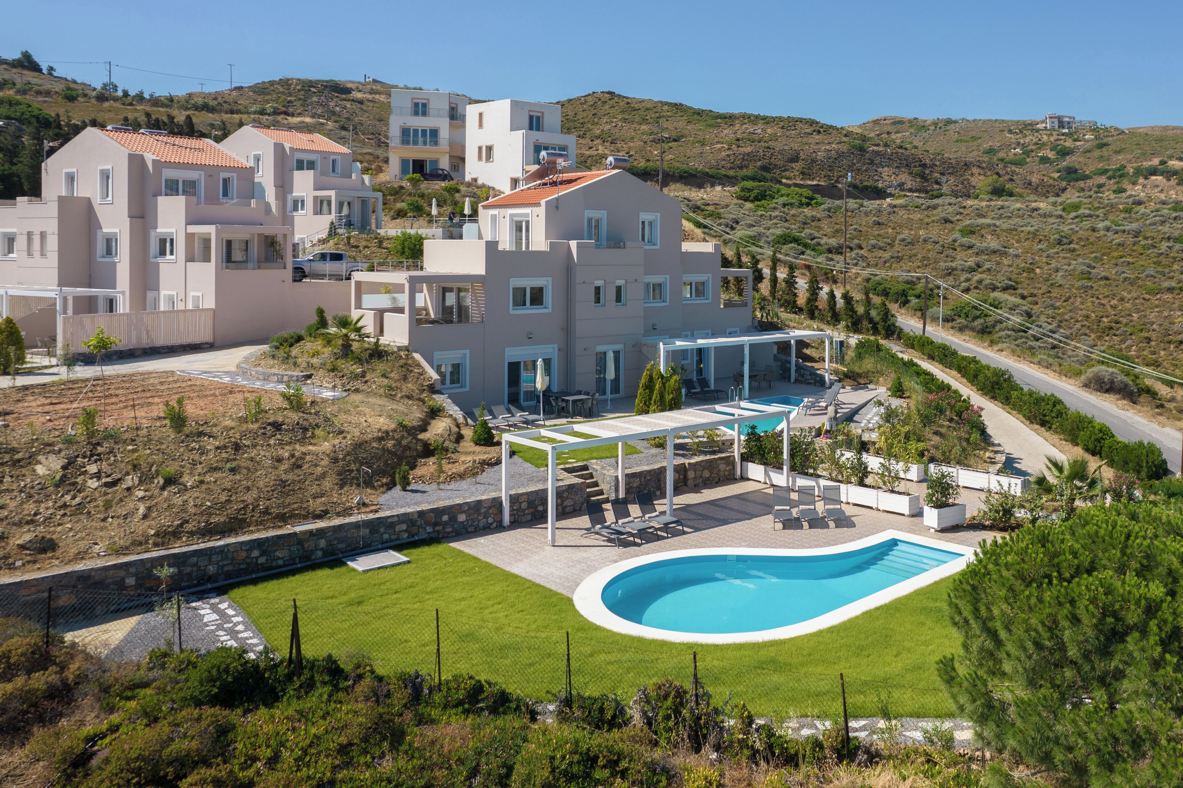 A modern villa with a swimming pool, a covered outdoor seating area, and a view of the surrounding hilly landscape.