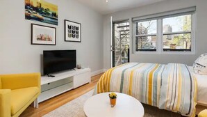 A modern bedroom with a bed, a TV, a sofa, and a window with a city view.