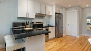 A modern kitchen with white cabinets, stainless steel appliances, and a wooden floor.