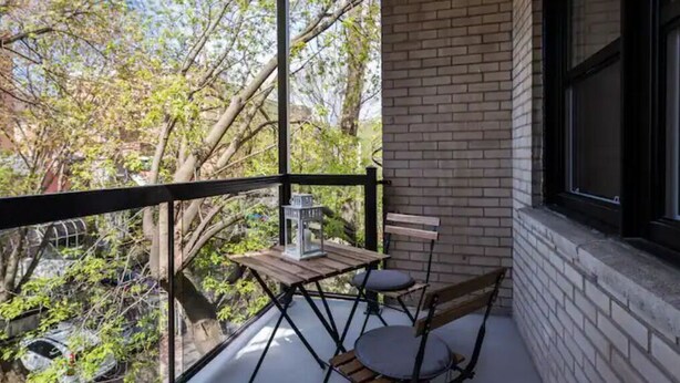A balcony with a wooden table and two chairs, overlooking a garden with trees and a car.