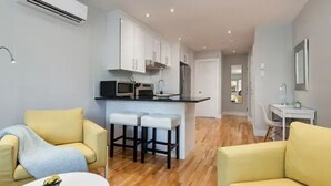 A modern apartment with a kitchen, two yellow sofas, a small dining table, and a white bar stool area.