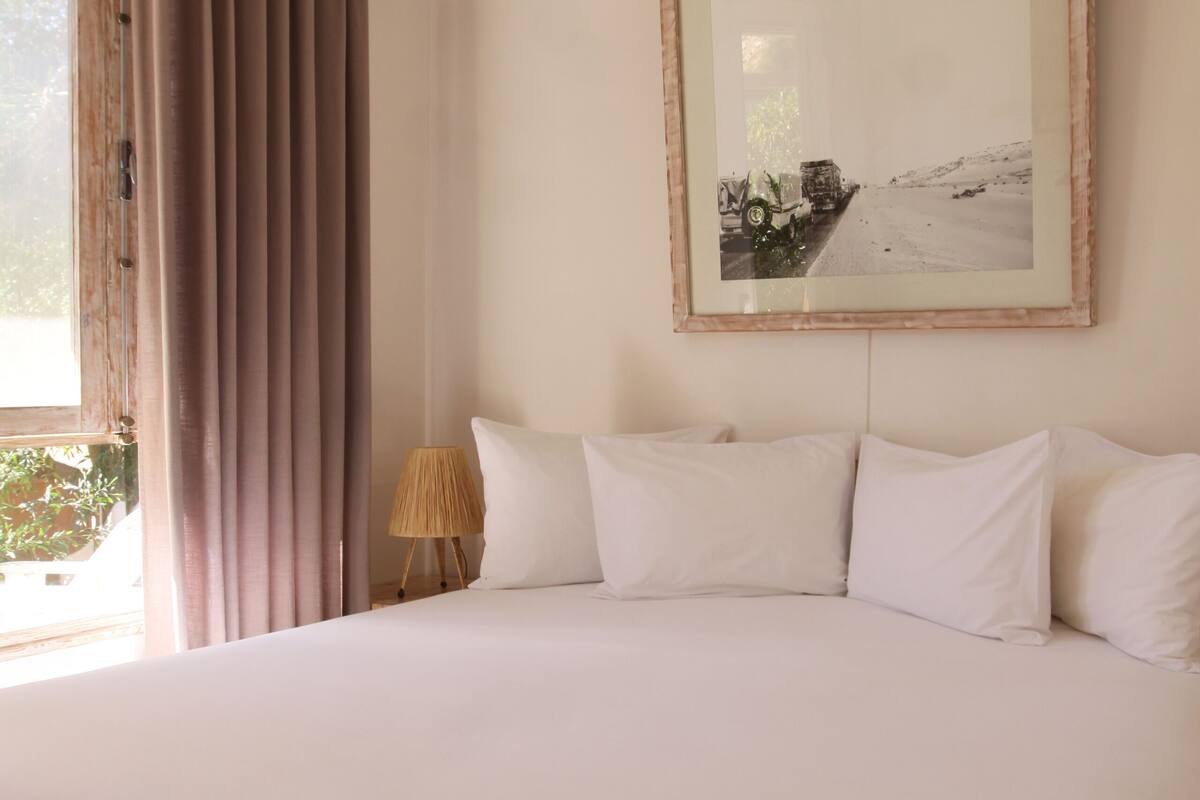 Uma cama grande com roupa de cama branca, uma cabeceira de madeira, um abajur e um quadro emoldurado na parede.