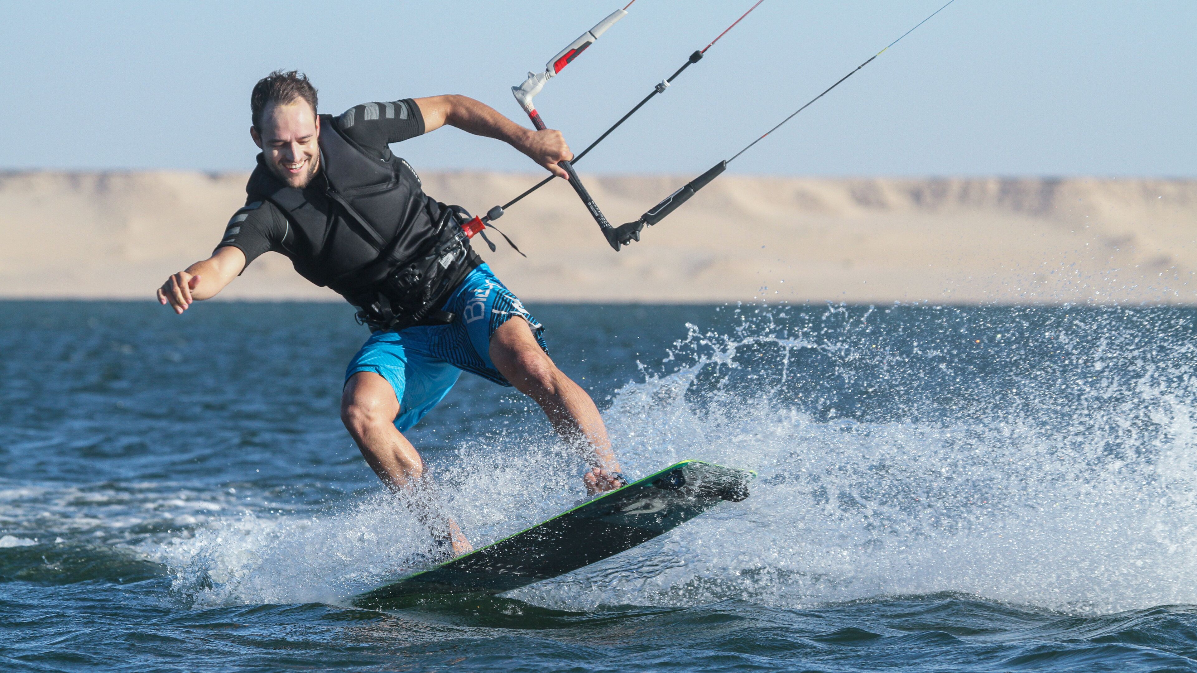 Una persona fa windsurf su un corpo d'acqua con una spiaggia sabbiosa sullo sfondo.