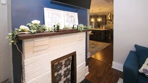 Un salon moderne avec une cheminée en briques blanches, un téléviseur à écran plat fixé au mur et des œuvres d’art décoratives.