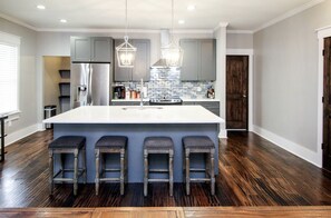 A modern kitchen with a large island, bar stools, stainless steel appliances, and a blue backsplash. - NoDa Updated Mill Home! Amazing Location- Walkable-Bars, Restaurants and Rail!
 (Charlotte)