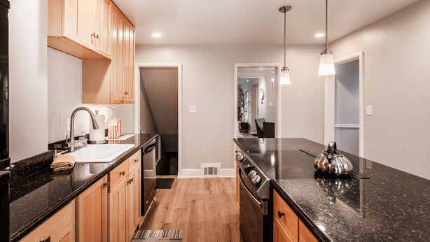 A modern kitchen with wooden cabinets, a black countertop, stainless steel appliances, and pendant lighting. - Cozy Downtown Retreat - Conference Center Home (Salt Lake City)