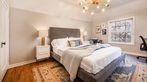 A bedroom with a bed, bedside tables, a lamp, a chair, a window, and a patterned rug. - Cozy Downtown Retreat - Conference Center Home (Salt Lake City)
