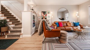 A modern living room with a staircase, a leather sofa, a round mirror, and a coffee table. - Cozy Downtown Retreat - Conference Center Home (Salt Lake City)